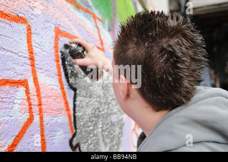 Teenage boy travaillant sur un morceau grafitti sur un mur extérieur. Banque D'Images