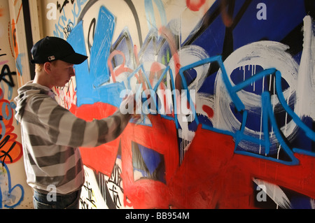 Teenage boy travaillant sur un graffiti sur un mur intérieur. Banque D'Images