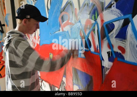 Teenage boy travaillant sur un graffiti sur un mur intérieur. Banque D'Images