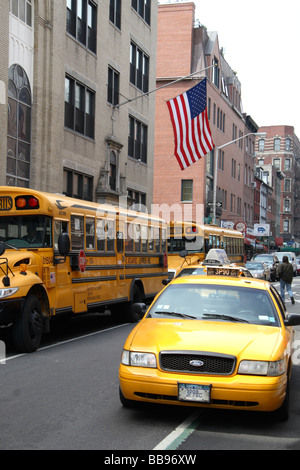 Les autobus scolaires jaunes américains traditionnels & taxi avec le Star Spangled Banner voler sur le bâtiment derrière. Banque D'Images