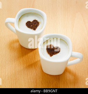 Deux tasses de café cappuccino style avec cœur des formes sur le dessus dans le chocolat en poudre. Banque D'Images