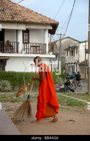 Le bouddhisme, un novice avec une robe rouge balayant le sol avec un balai en face de l'Sudharmalaya Temple, Fort de Galle, Ceylan, Sri Banque D'Images