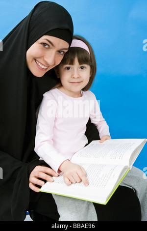 Une mère portant un hijab et sa fille lire un livre Banque D'Images