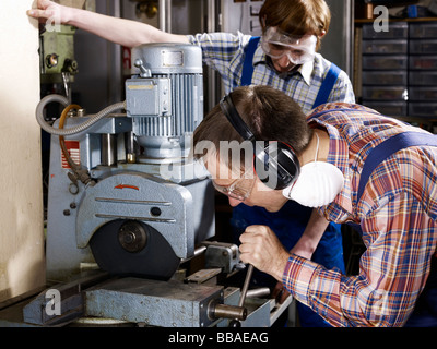 Un homme à l'aide d'une scie électrique dans un atelier tandis qu'un jeune homme regarde sur Banque D'Images