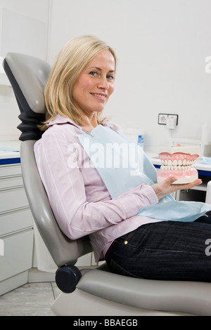 Une femme assise dans un fauteuil dentaire et les dents modèles holding Banque D'Images