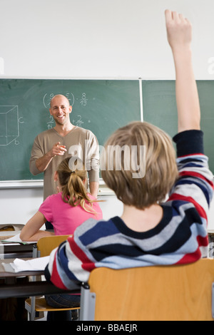 Vue arrière d'un garçon levant la main dans une salle de classe Banque D'Images