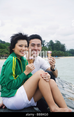 Couple assis sur le brise-lames, eating ice cream Banque D'Images