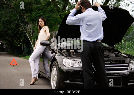 L'homme à la recherche sous un capot de voiture de voiture en panne, woman waiting Banque D'Images