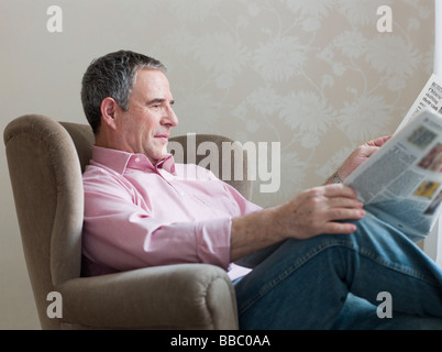 Man reading paper sitting in chair Banque D'Images