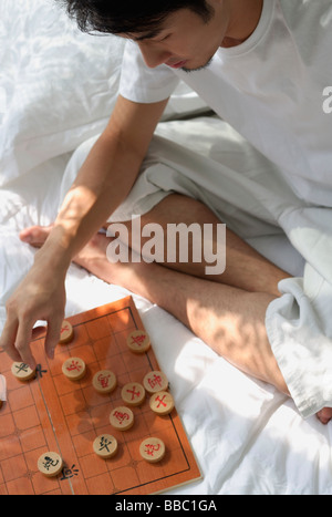 Jeune homme assis sur le lit, jouant aux échecs chinois Banque D'Images