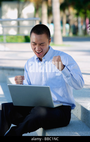 Un homme est excité comme il utilise son laptop outdoors Banque D'Images