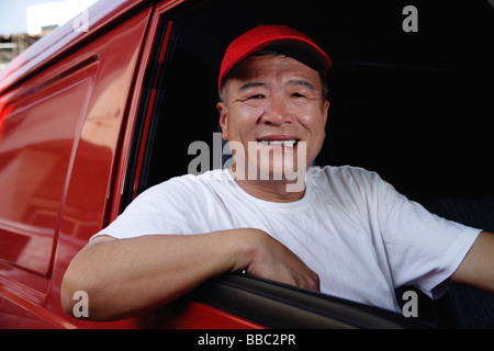 Un homme dans un van rouge sourit à l'appareil photo Banque D'Images