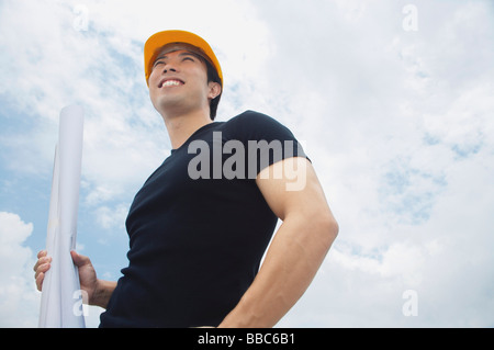 Jeune homme dans l'exécution de plans, hardhat, smiling Banque D'Images