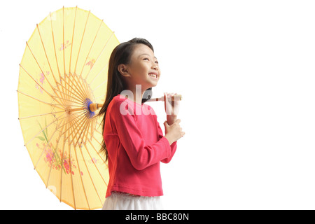 Girl holding yellow umbrella, standing against white background Banque D'Images