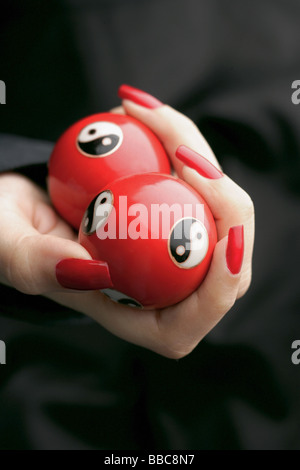 Womans mains avec du vernis à ongles rouge, holding Yin Yang balls Banque D'Images