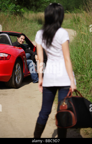 Femme debout sur le côté de la route, à la recherche de l'homme en voiture sport rouge Banque D'Images