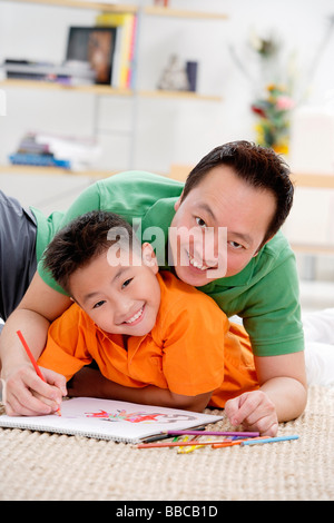 Père et fils à la maison, allongé au sol avec Sketch Pad, smiling at camera Banque D'Images
