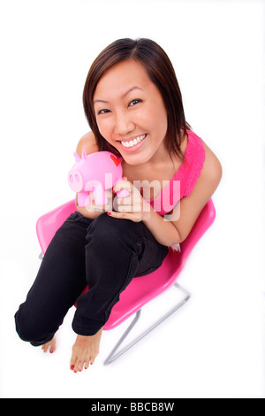 Jeune femme assise sur une chaise, holding piggy bank, smiling Banque D'Images