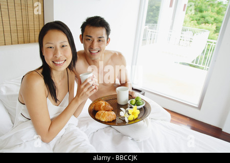 Couple having breakfast in bed, looking at camera Banque D'Images
