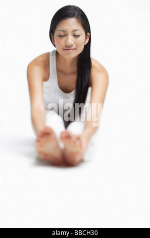 Woman doing yoga, assis sur le plancher, l'étirement, tenant les pieds, les yeux fermés Banque D'Images
