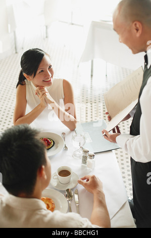 Waiter showing menu pour deux au restaurant, la femme en lui souriant Banque D'Images