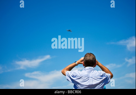 Vue arrière de l'homme regardant à travers des jumelles à un avion militaire dans un ciel bleu à la riat Gloucestershire Angleterre Royaume-uni Fairford Banque D'Images