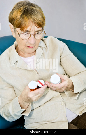 Femme âgée la lecture des étiquettes d'avertissement sur les bouteilles de pilules à l'aide de médicaments Banque D'Images