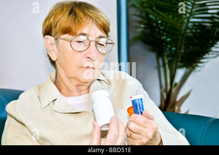 Femme âgée la lecture des étiquettes d'avertissement sur les bouteilles de pilules à l'aide de médicaments Banque D'Images