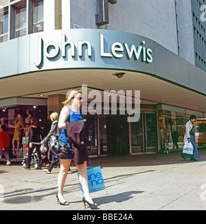 Une jeune femme passe devant l'entrée du grand magasin John Lewis Au printemps, avec un sac de shopping sur Oxford Street, Londres, Angleterre ROYAUME-UNI Banque D'Images