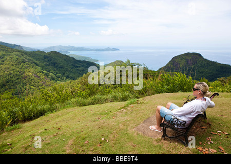 Femme assise sur un banc à l'Morone National Park, plage de Grand'Anse à l'arrière, l'île de Mahé, Seychelles, océan Indien, Afrique Banque D'Images