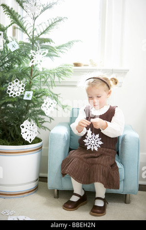 Petite fille décorer un arbre de Noël avec des flocons de papier Banque D'Images