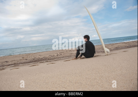 Young man sitting on beach with his surfboard Banque D'Images