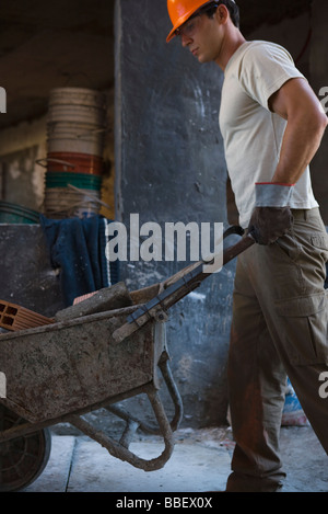 Construction Worker pushing wheelbarrow par construction site Banque D'Images