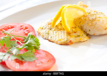 Filet de poisson grillé garni de citron et de salade de tomates fraîches. Banque D'Images