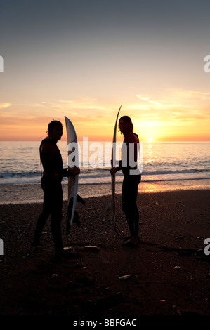 Deux jeunes hommes tenant leurs planches de surf sur le point d'aller faire du surf au coucher du soleil au large de la plage d'Aberystwyth Wales UK Banque D'Images