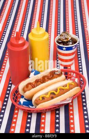Une table de pique-nique avec un chiffon tableau patriotique héberge un panier de hot-dogs avec du ketchup et de la moutarde et un froid soday bouteilles Banque D'Images