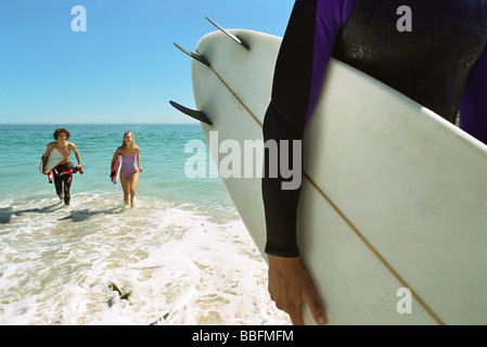 Surfer carrying board sous le bras, un couple sortant d'eau ensemble Banque D'Images