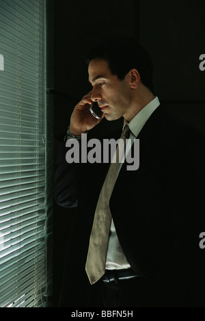 Businessman using cell phone, regardant à travers la fenêtre de stores Banque D'Images