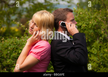 Jeune femme et un jeune homme debout dos à dos tout en parlant sur un téléphone mobile Banque D'Images