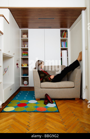 Jeune fille assise sur le fauteuil dans sa chambre Banque D'Images