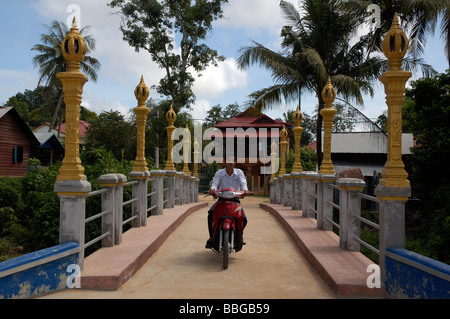 Garçon cambodgien sur une conduite motorbyke passant par un pont à Siem Reap, Cambodge Banque D'Images