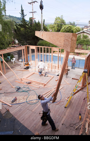 La poutre faîtière géant étant détenu par une grue et pivoté en position par un menuisier à un travail de construction résidentielle rénovation Banque D'Images