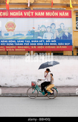 Ninh Binh "scène de rue", 2 filles riding bike sous affiche de communiste, Vietnam, Asie du Sud-Est [] Banque D'Images