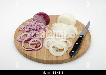 Oignons rouges et blancs (Allium cepa), pelées, coupées en dés les oignons, les rondelles d'oignon sur une planche en bois, avec un couteau Banque D'Images