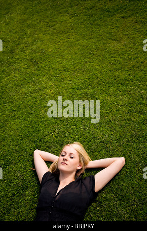 Une jeune femme s'allonge sur l'herbe de soleil, de détente, de réflexion ou simplement se reposer dans la chaleur du soleil. Banque D'Images