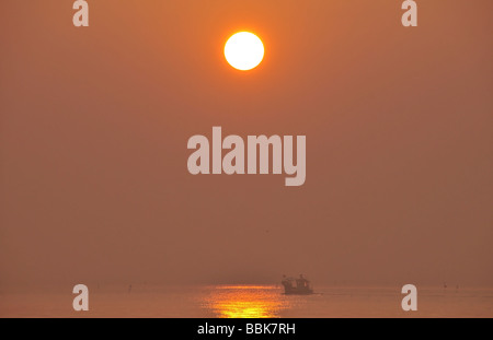 Lever du soleil rouge sur une mer calme avec un petit bateau de pêche au homard pot traversant une red sun glow à Lido di Jesolo, Italie Banque D'Images