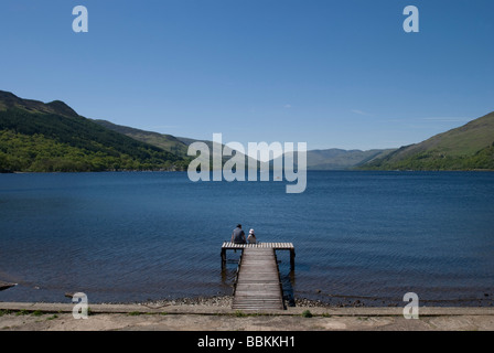 Père et fille assise sur une jetée à St Fillans sur le Loch Earn, en Écosse. Banque D'Images