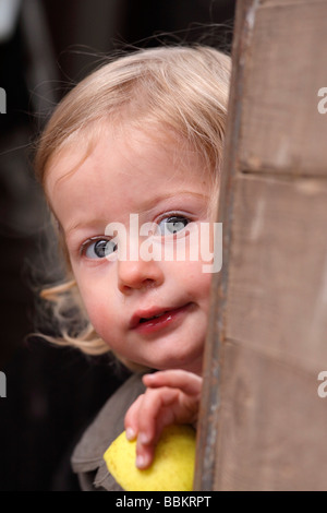 Portrait d'une petite fille, curieusement, à la recherche autour d'un coin. Banque D'Images