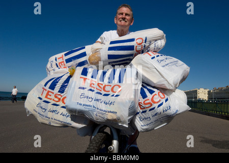 Un homme de retour de shopping à Tesco sur un vélo avec chargés de sacs en plastique plein d'épicerie. Banque D'Images