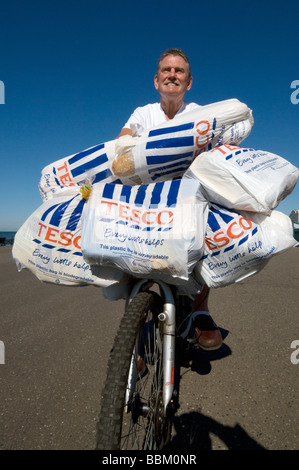 Un homme de retour de shopping à Tesco sur un vélo avec chargés de sacs en plastique plein d'épicerie. Banque D'Images